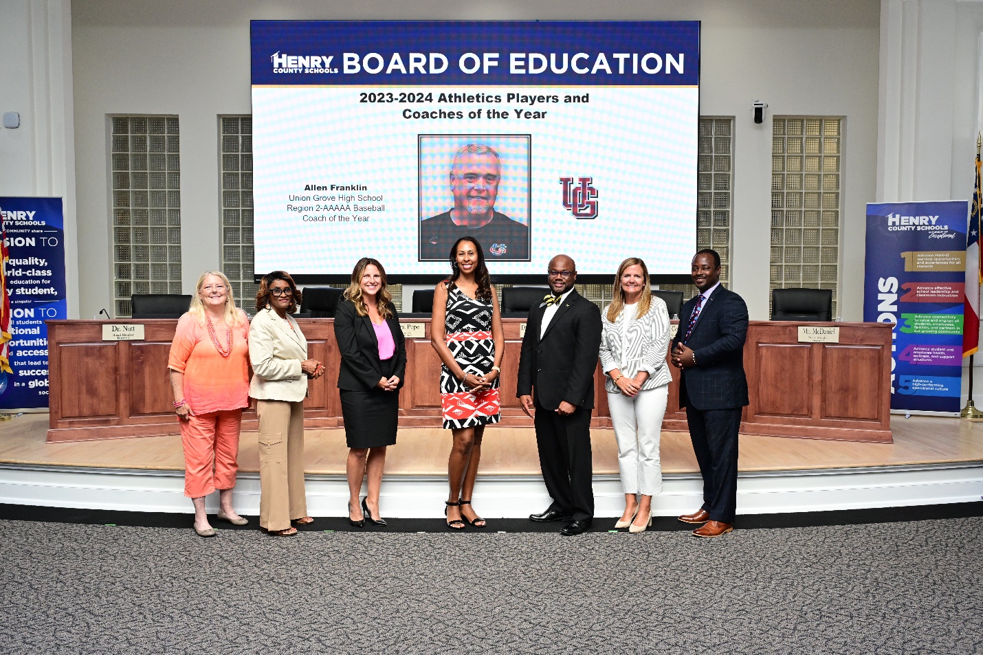 A group of people standing in front of a large screenDescription automatically generated